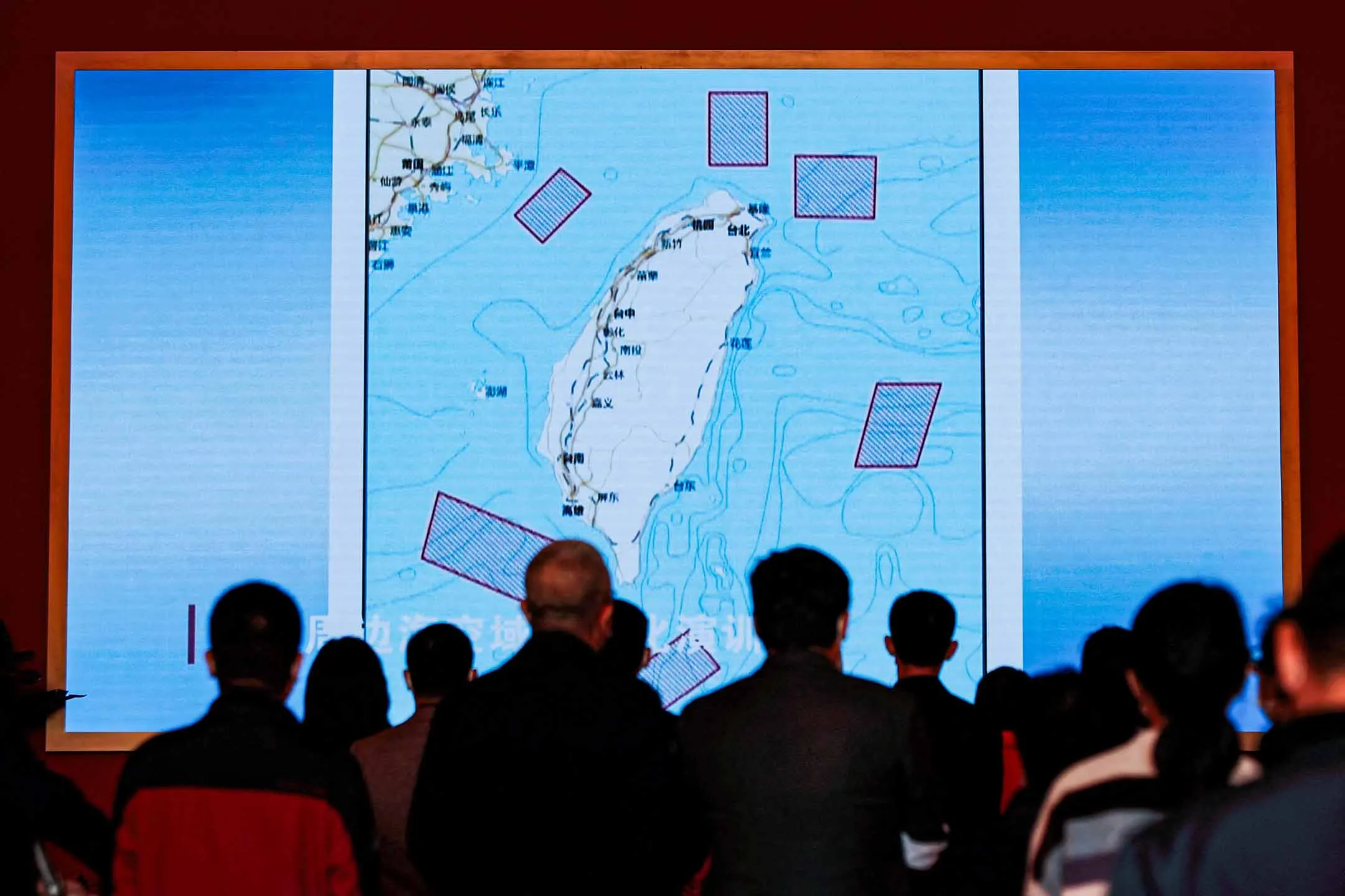 2022年10月12日，北京，人們站在一個巨大的屏幕前，上面顯示中國人民解放軍在台灣進行軍事演習的地點。
